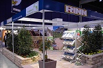 Gemeinsam mit der Firma Rinn gestaltete unser Unternehmen einen Stand auf der Dresdner Baumesse. Zu sehen sind randbegrenzende Beete aus gelben und rötlichen Betonformsteinen, die mit etwa 1,2 m hohen belaubten Sträuchern bepflanzt wurden. Auf dem Boden des Messestandes wurden farbige Betonplatten verlegt. Metallständer mit Adikawerbung umfassen den gesamten Messestand. Prospektaufsteller aus Metall und großflächige Farbfotos ergänzen die Gestaltung.